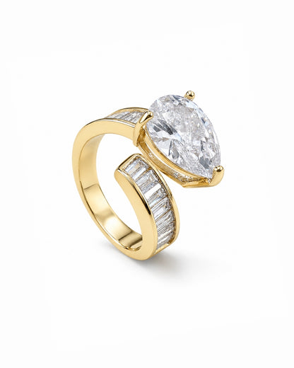 A yellow gold ring featuring a large pear-cut clear center stone and channel-set clear stones along the band, shown on a clean white background.