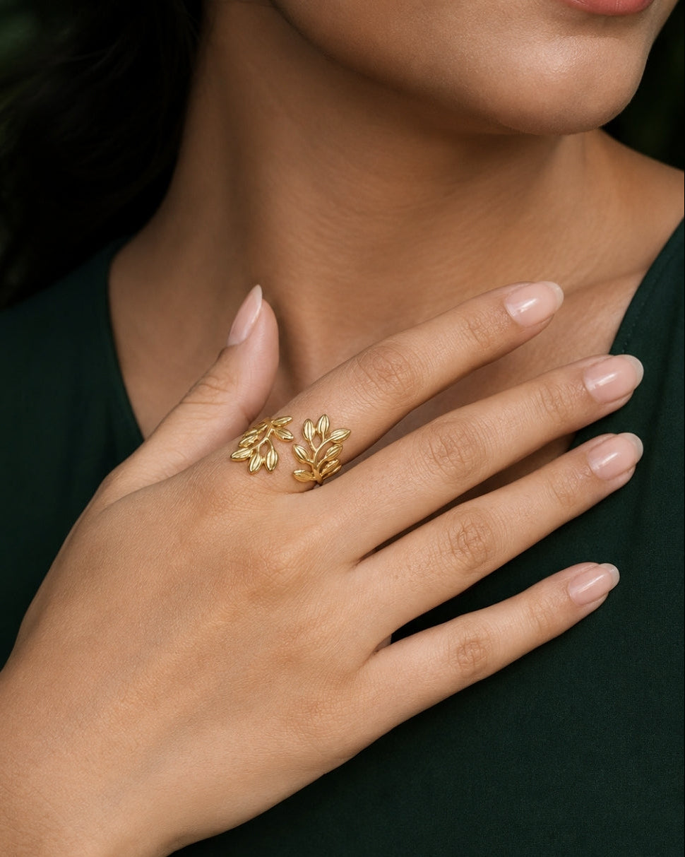 A close-up of a person's hand wearing a delicate gold ring with a small leaf or vine motif, set against a dark green sleeveless top.