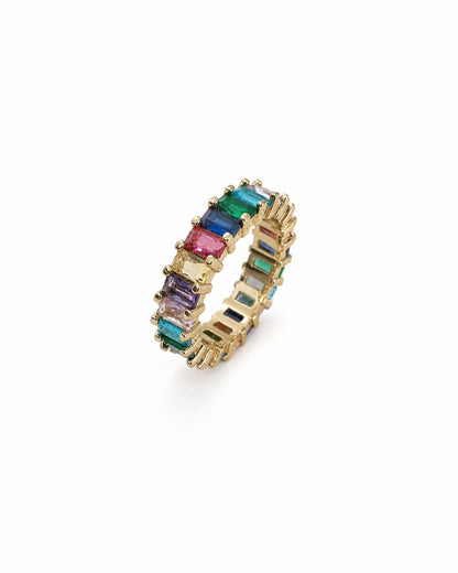 A gold eternity ring featuring a row of colorful baguette-cut gemstones, including pink, blue, green, and purple, set against a plain white background.