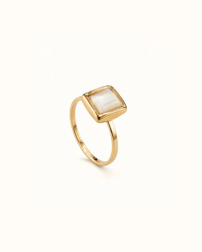 A gold ring with a square bezel-set white mother-of-pearl stone, shown on a clean off-white background.