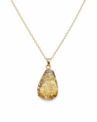 A gold chain necklace with a teardrop-shaped druzy pendant featuring a textured, crystalline yellow and gold surface, set against a plain white background.