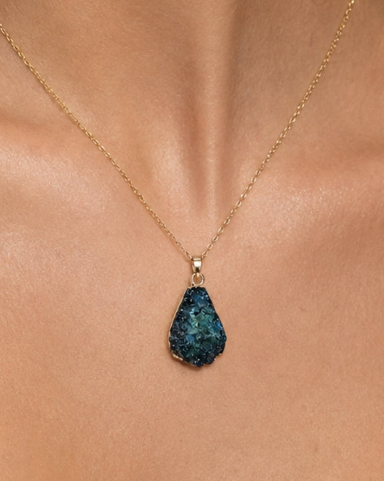 A gold chain necklace with a teardrop-shaped dark blue textured stone pendant, worn on a model's neck.